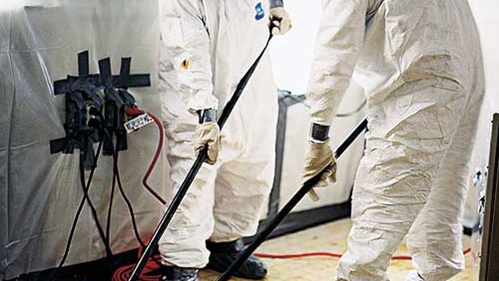 Two men in an asbestos abatement crew removing asbestos from the floor of a home.